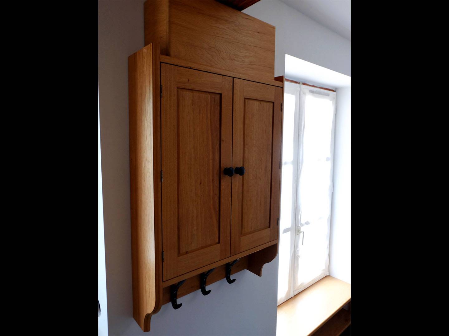 Petit placard suspendu faisant partie de l'ensemble mobilier d'une pièce. Intégration de porte-manteaux. Fabrication en chêne massif. Atelier de la baleine. 2023