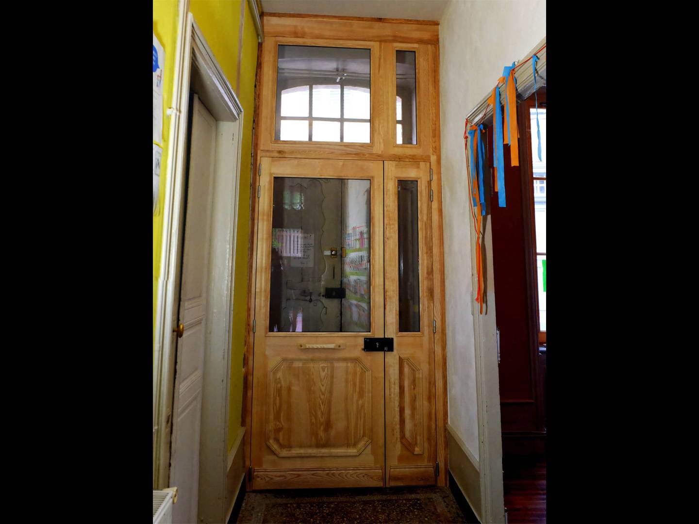 Porte d'entrée pour un sas d'immeuble. Fabriquée entièrement en frêne, moulure à grand cadre, imposte et ornementation. Atelier de la baleine. 2025