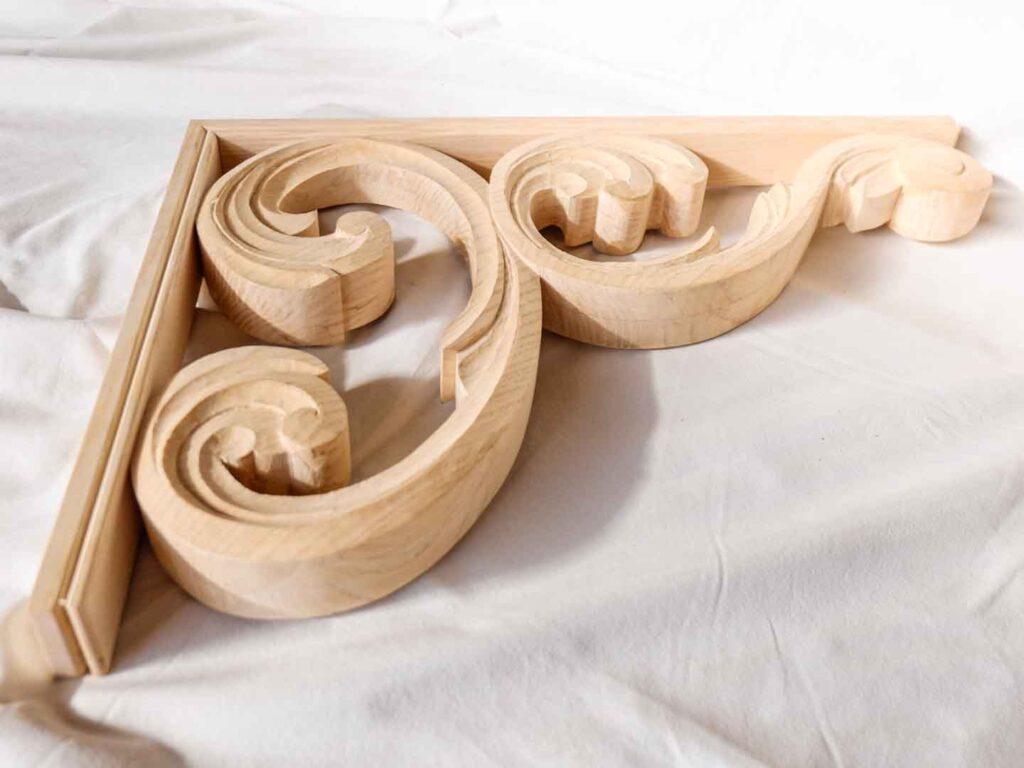Corniches sculptées dans du frêne massif. Elles sont installées dans le prolongement de la structure d'un auvent. Atelier de la baleine. 2023