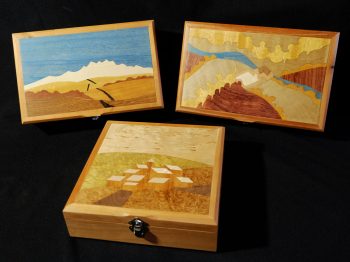 Boites à secret ornées d'une marqueterie de paysage imaginaire. La structure apparente est en merisier et les placages intérieurs sont en loupe d'amboine et ronce de noyer. Atelier de la baleine. 2026.