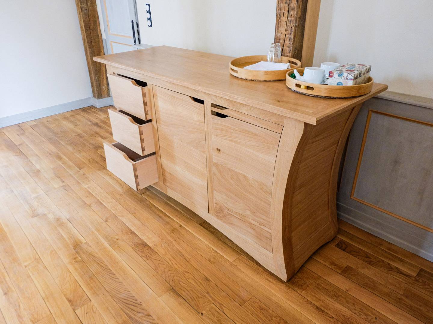 Comptoir contemporain galbé. Grand meuble de salle à manger, entièrement en chêne massif. Panneaux massifs cintrés. Portes sur pivots, tiroirs découpés selon le galbe, et tablette. Meuble déplaçable sur roulettes. Atelier de la baleine. 2023