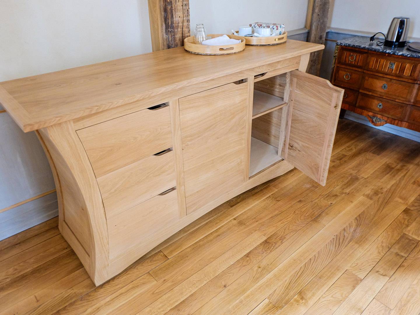Comptoir contemporain galbé. Grand meuble de salle à manger, entièrement en chêne massif. Panneaux massifs cintrés. Portes sur pivots, tiroirs découpés selon le galbe, et tablette. Meuble déplaçable sur roulettes. Atelier de la baleine. 2023