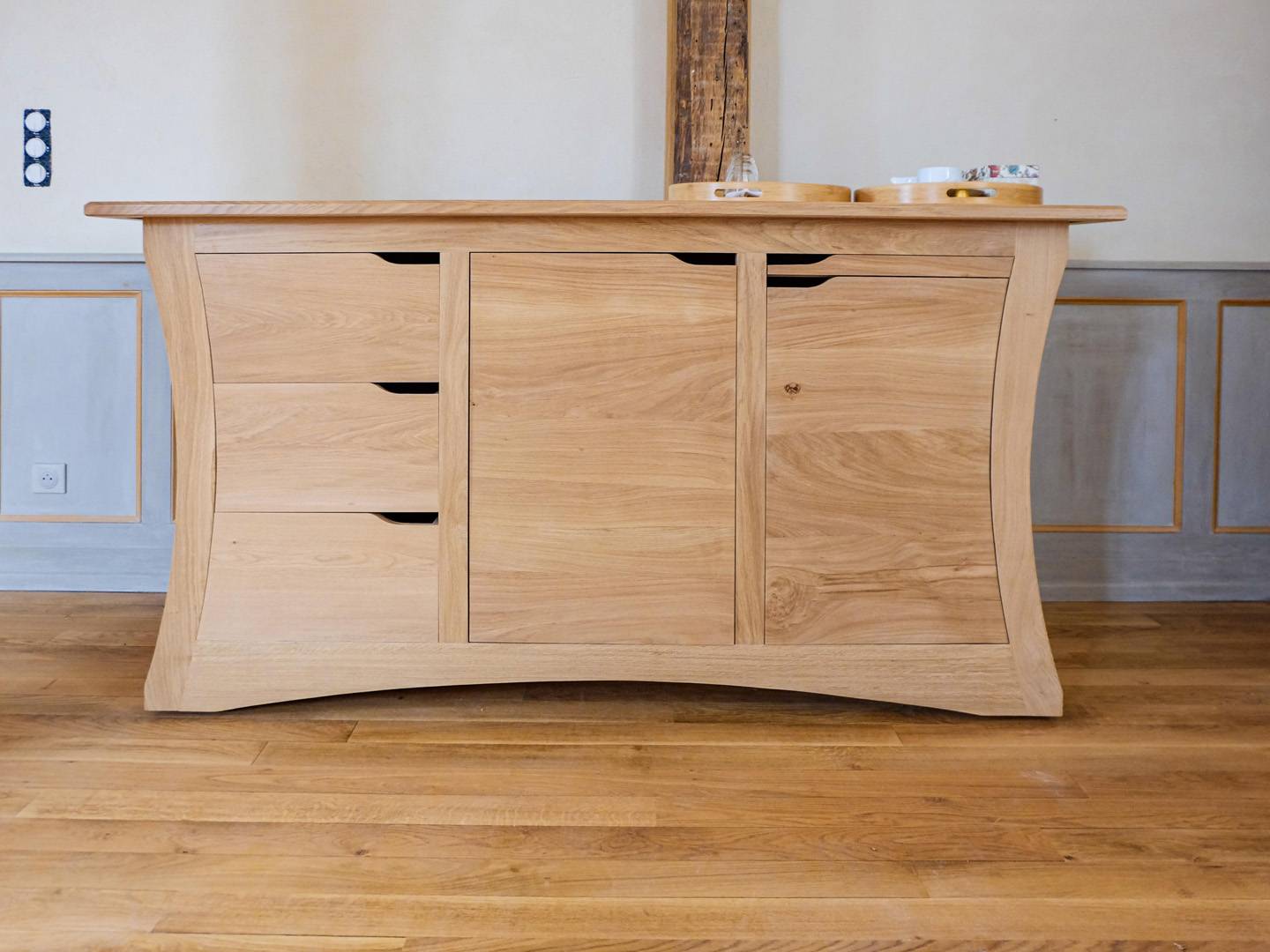 Comptoir contemporain galbé. Grand meuble de salle à manger, entièrement en chêne massif. Panneaux massifs cintrés. Portes sur pivots, tiroirs découpés selon le galbe, et tablette. Meuble déplaçable sur roulettes. Atelier de la baleine. 2023