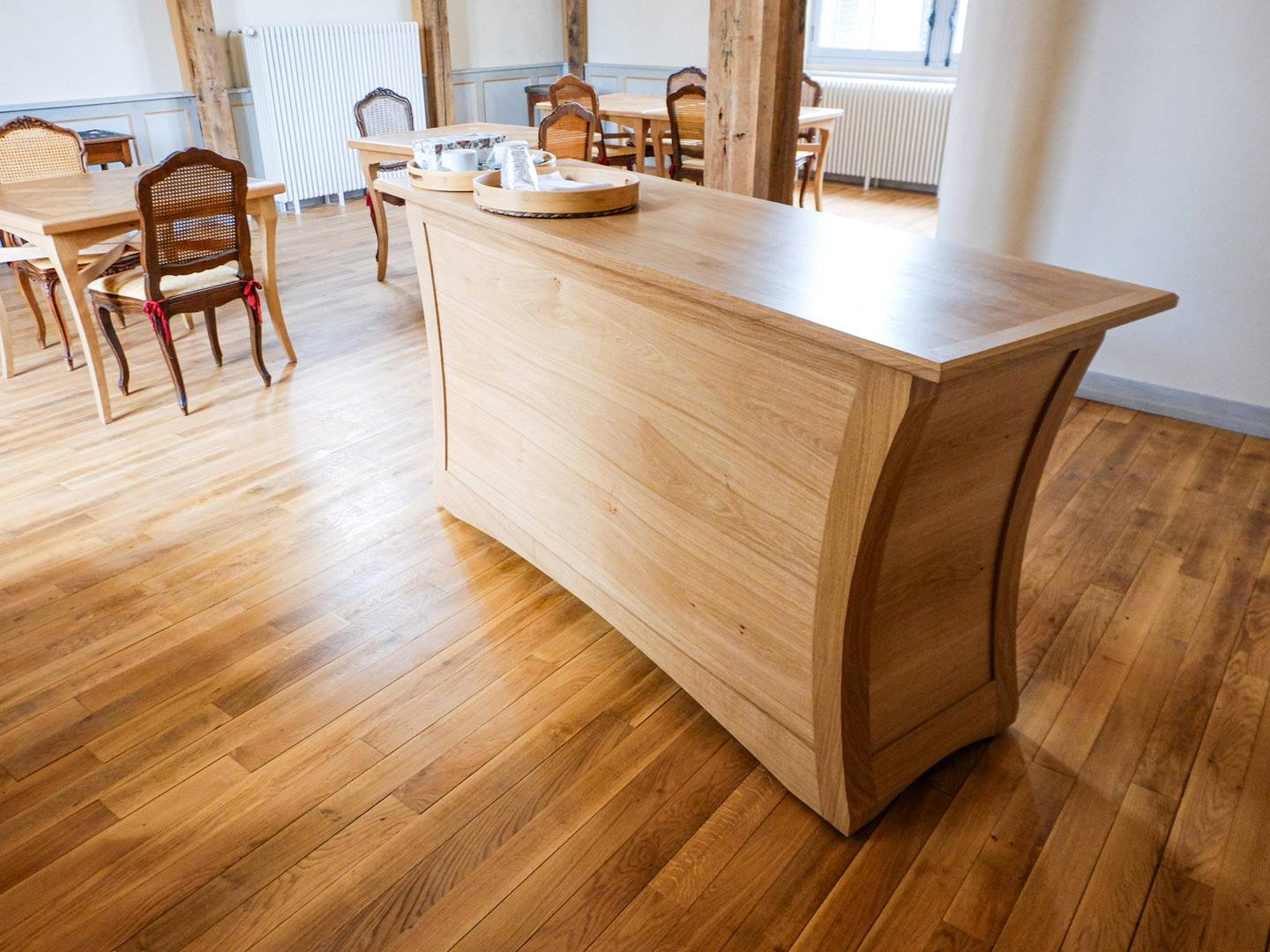 Comptoir contemporain galbé. Grand meuble de salle à manger, entièrement en chêne massif. Panneaux massifs cintrés. Portes sur pivots, tiroirs découpés selon le galbe, et tablette. Meuble déplaçable sur roulettes. Atelier de la baleine. 2023